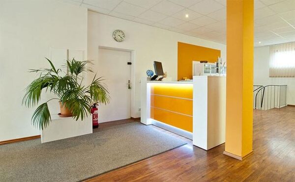 Heller Empfangsbereich mit modernem Tresen, Zimmerpflanze und freundlicher Atmosphäre.